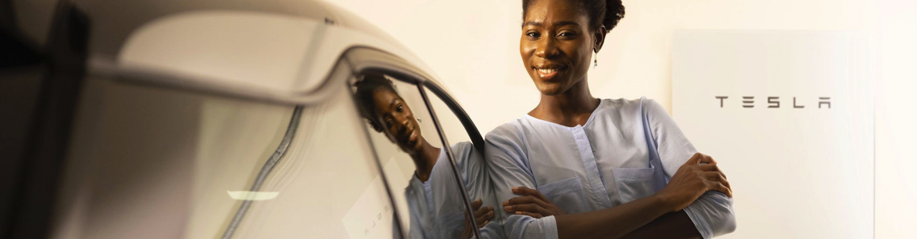 woman standing in front of tesla battery next to a car